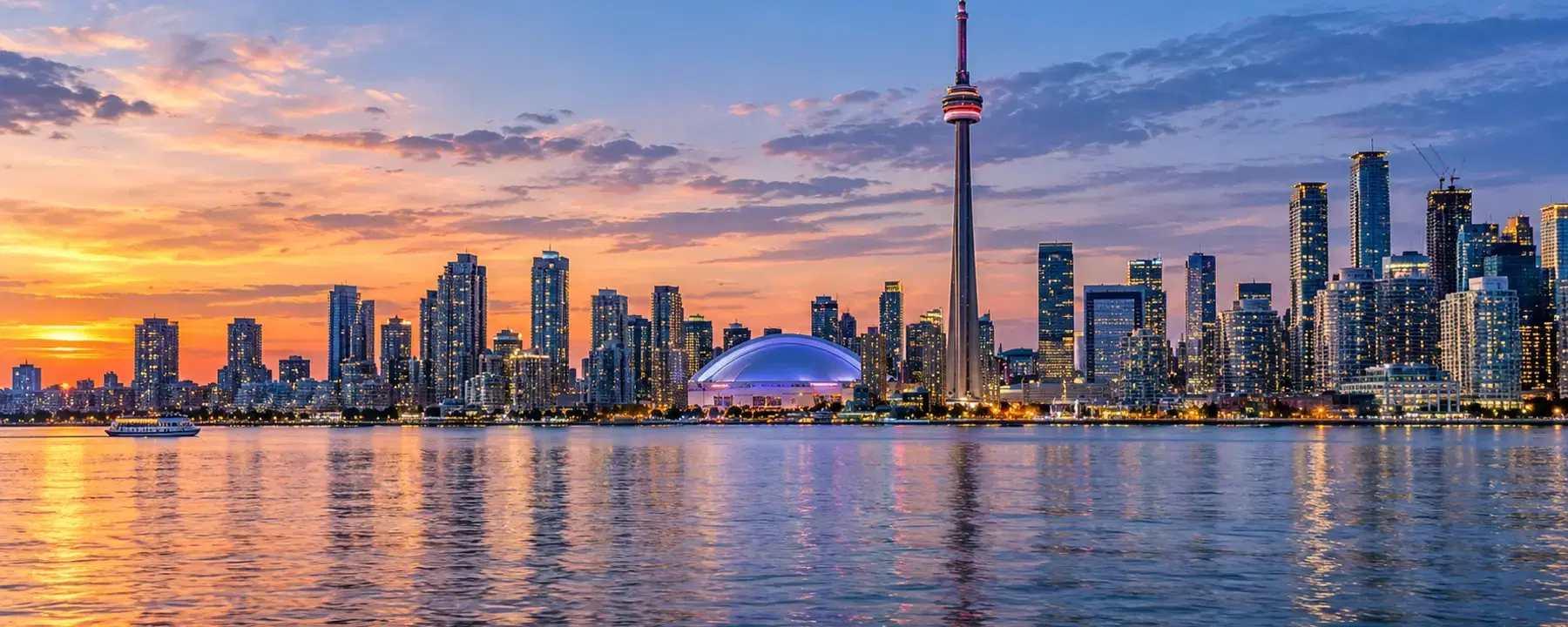 A city skyline at sunset across open water, with a domed stadium at the right.