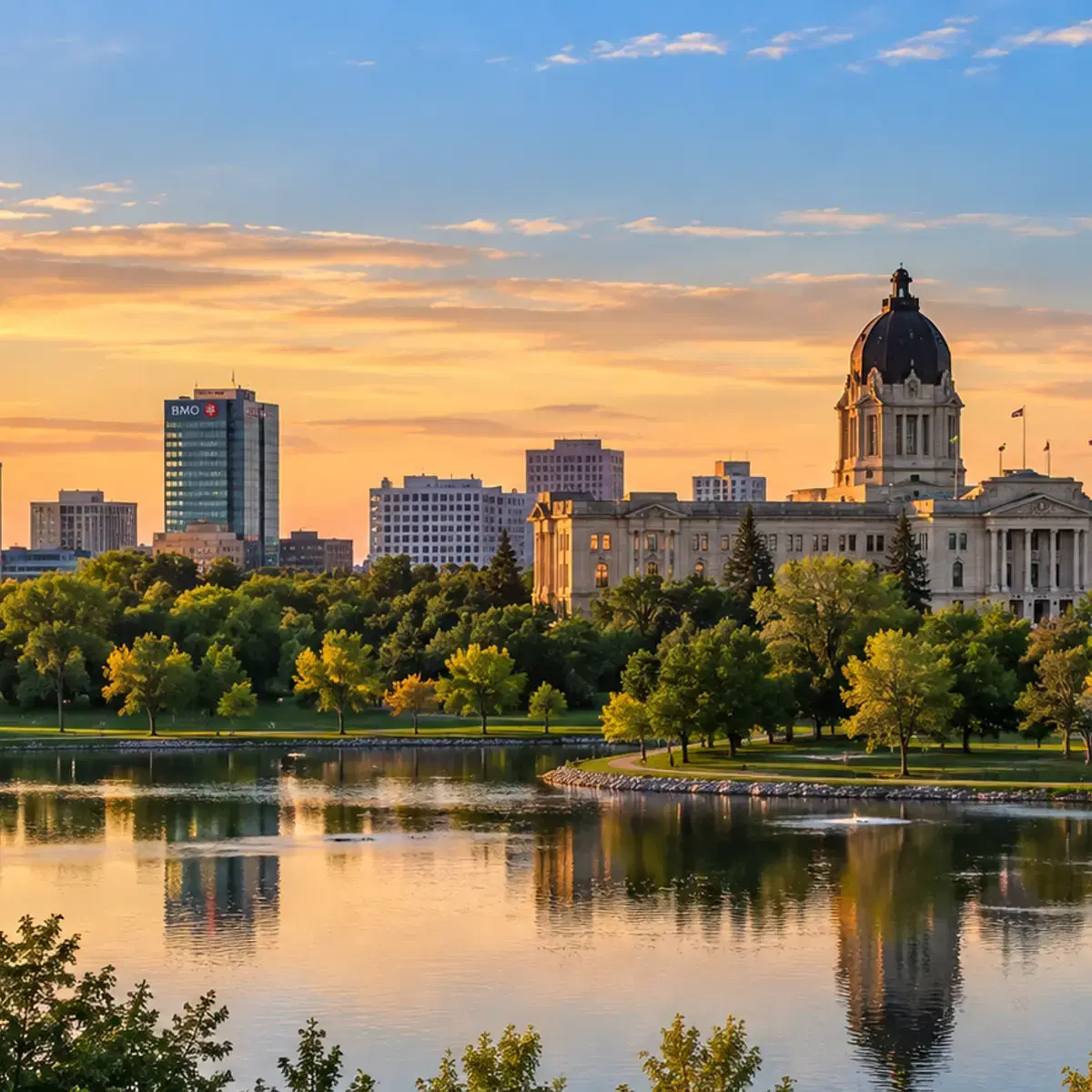 A domed legislature building and city skyline at sunset, reflected in a lake.