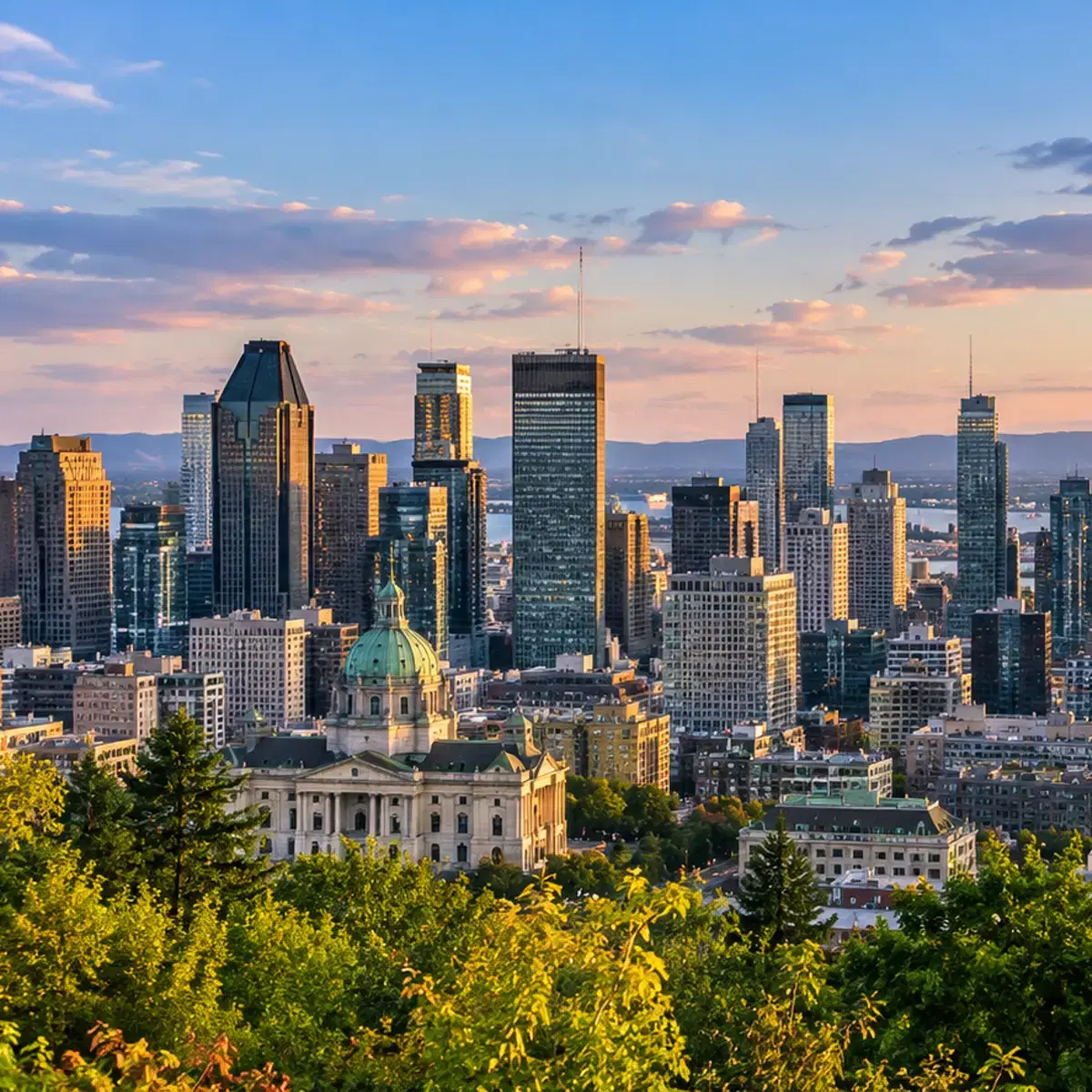 A city skyline at sunset seen from a wooded hillside, with a green-domed cathedral below.